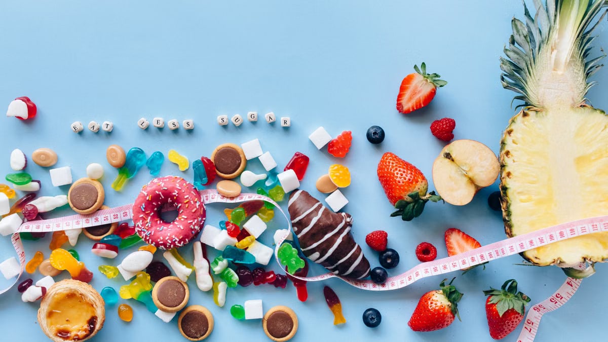 Flat lay of sweets and fruits on blue background with health message 'Eat Less Sugar'.